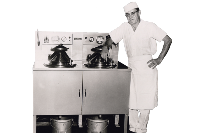 Historic black and white photo of a man in an apron standing by two Broaster pressure fryers